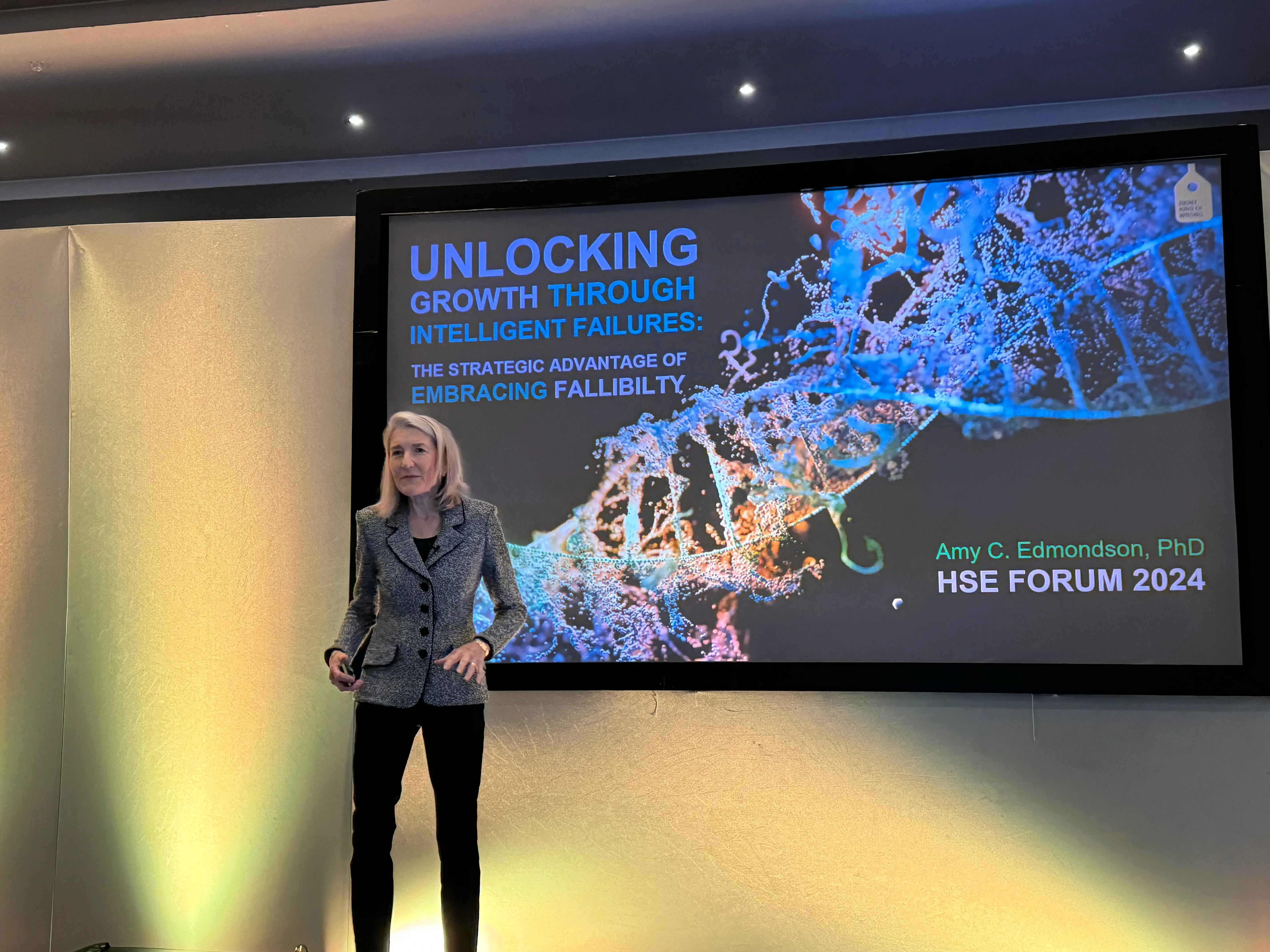 A female with blonde hair stood on a stage presenting slides on AI.