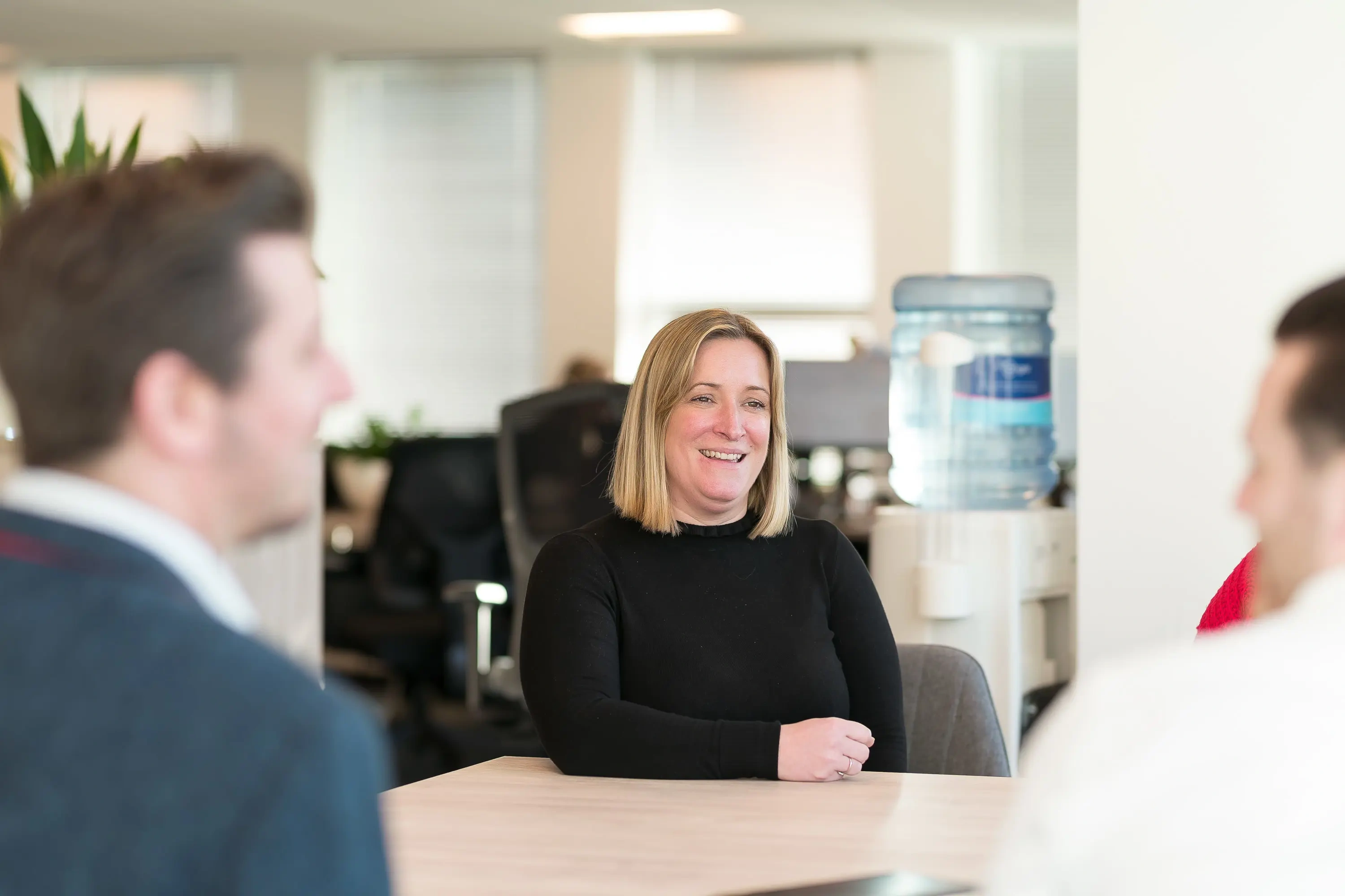 A smiling woman sat at a desk in a meeting.